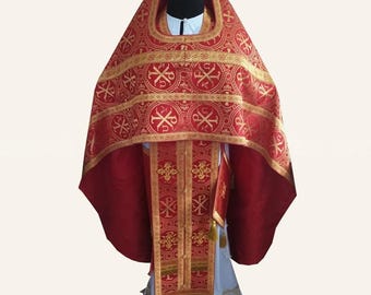 May include: A red and gold liturgical vestment set featuring a wide, ornate phelonion with Chi Rho symbols and a matching sticharion. The garment includes a long, rectangular red stole with gold embroidery and a white base layer with gold trim.