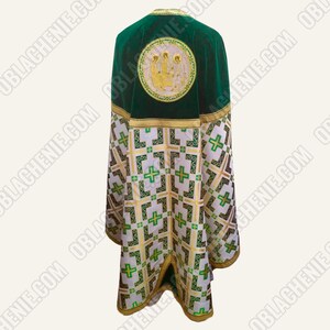 May include: A green and white liturgical vestment with gold accents. The back features a circular embroidered design with figures. The lower portion has a repeating pattern of crosses and geometric shapes.