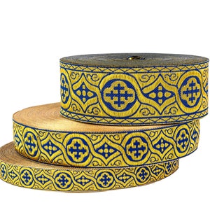 Puede incluir: Tres rollos de ribete dorado y azul con un diseño de cruz. El ribete está tejido con un patrón repetido de cruces y formas geométricas.