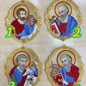 Op de afbeelding: Vier geborduurde patches met religieuze figuren in ovale frames met gouden versieringen. Elke patch heeft een andere figuur en symbool, waaronder een leeuw, een boek, een engel en een stier. De patches zijn genummerd van 1 tot 4.