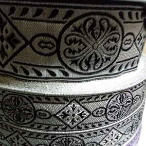 May include: Stack of silver and black patterned fabric trim with a blue and silver trim on top.