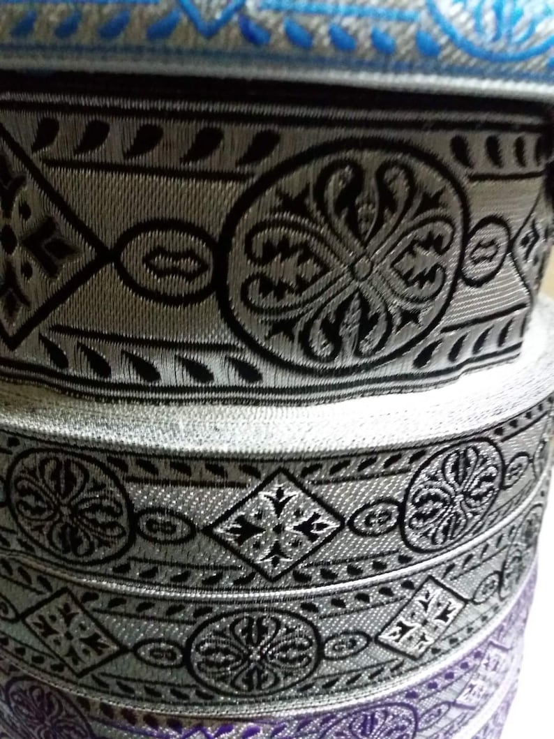May include: Stack of silver and black patterned fabric trim with a blue and silver trim on top.