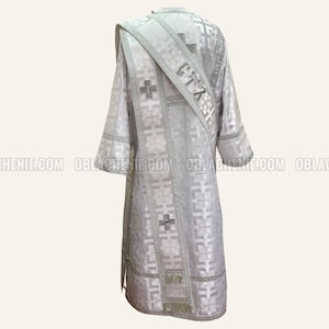 May include: A white liturgical vestment with a silver embroidered cross and the word "Christ" on the sash. The vestment has a geometric pattern and is made of a silky fabric.