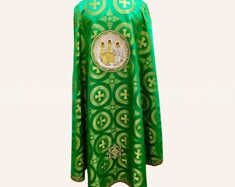 May include: A bright green liturgical vestment featuring a repeating gold cross pattern and a central circular medallion depicting three figures. The garment has a structured, flowing silhouette with gold trim along the bottom hem.