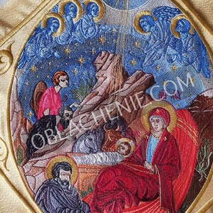 Puede incluir: Icono religioso bordado que representa la escena de la Natividad. El icono presenta un fondo dorado con un marco circular y una representación detallada de María, José y el niño Jesús en un pesebre. La escena se desarrolla sobre un fondo de cielo estrellado con ángeles en la parte superior del icono.