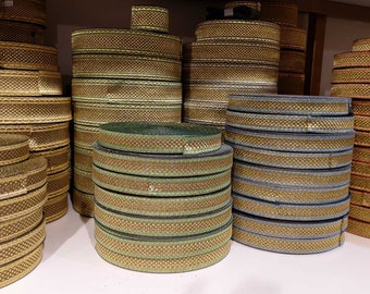 Puede incluir: Pilas de ribetes dorados, verdes y azules con un patrón tejido. Los ribetes están dispuestos en filas sobre una superficie blanca.