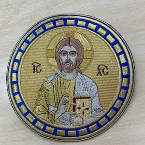 May include: Embroidered patch featuring a gold and white image of Jesus Christ holding a book. The patch is surrounded by a blue and gold border.
