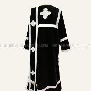 May include: Black velvet robe with white embroidered details. The robe has a long, flowing design with a white trim around the edges. The embroidery features a cross pattern.