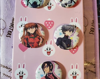 May include: Six pink and white button pins featuring anime characters from the show Neon Genesis Evangelion. The characters are Rei Ayanami, Asuka Langley Soryu, Shinji Ikari, and Misato Katsuragi. The pins are arranged in a grid pattern on a pink background with white bunny and strawberry designs.
