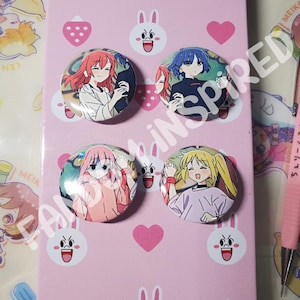 May include: Four round button pins featuring anime characters. The pins are on a pink background with white bunny and heart designs.