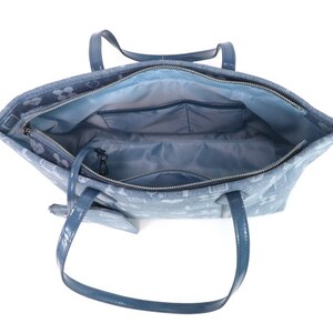 Puede incluir: Un bolso tote azul claro con un patr&oacute;n blanco. El bolso tiene una cremallera y dos asas superiores. El bolso est&aacute; abierto y el interior est&aacute; forrado con un tejido azul claro. Hay un peque&ntilde;o bolsillo con cremallera en el interior del bolso.