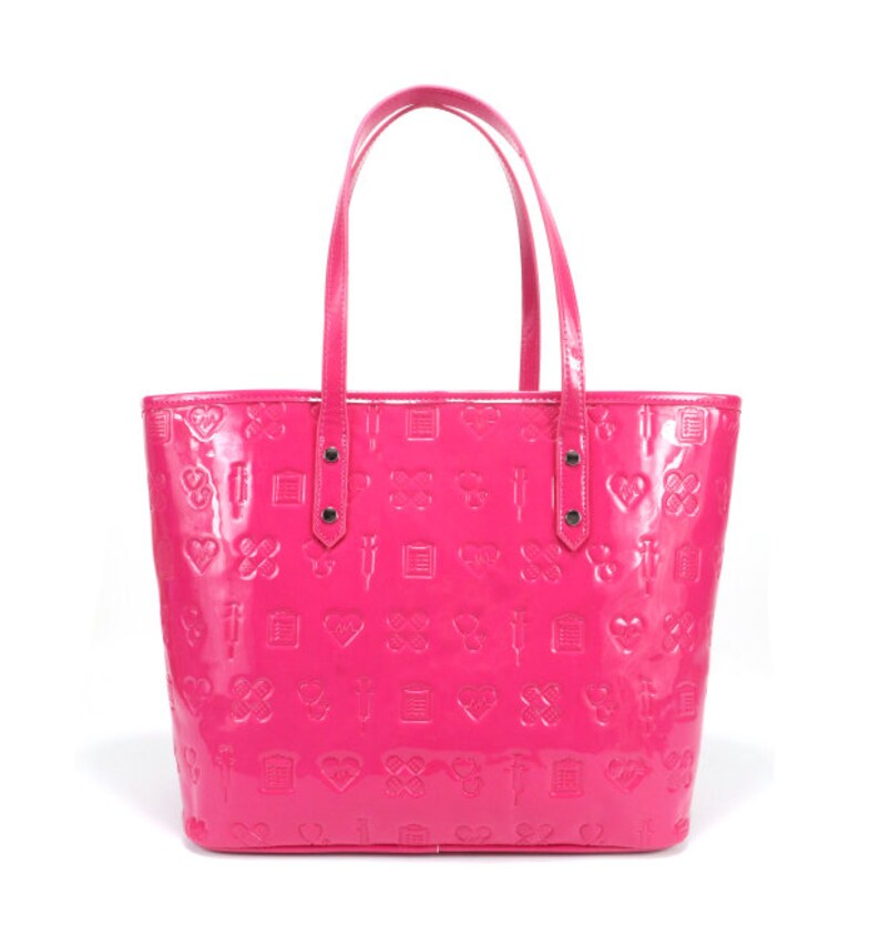 Puede incluir: Un bolso tote de color rosa brillante con un acabado brillante. El bolso tiene un patr&oacute;n de corazones, cruces y otros s&iacute;mbolos en relieve en la superficie.