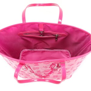 Puede incluir: Un bolso tote de charol rosa con un bolsillo con cremallera y un peque&ntilde;o bolsillo interior. El bolso tiene un patr&oacute;n de monograma.