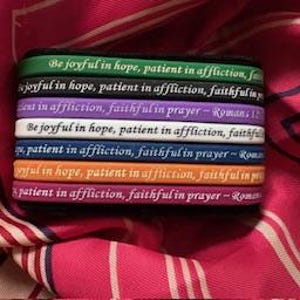May include: A stack of colorful silicone bracelets with the Bible verse "Be joyful in hope, patient in affliction, faithful in prayer - Romans 12:12" printed on them.