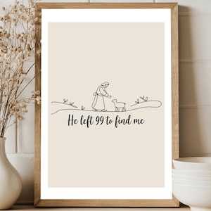 May include: A framed print featuring a minimalist line drawing of a person with a lamb. The artwork is set against a beige background, with the text "He left 99 to find me" in a script font. The frame is light brown.
