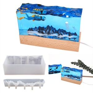 May include: A clear resin mold with a wooden base, featuring a scuba diver, mountains, and jellyfish. The mold is designed for creating a resin art piece with a 3D effect. The mold is shown with a finished resin piece.