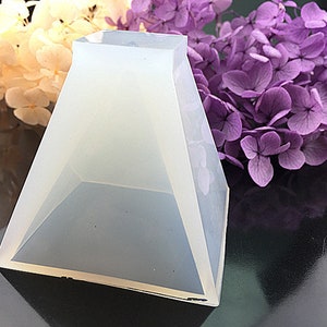 Op de afbeelding: Een transparante siliconen mal in de vorm van een piramide. De mal ligt op een zwart oppervlak.