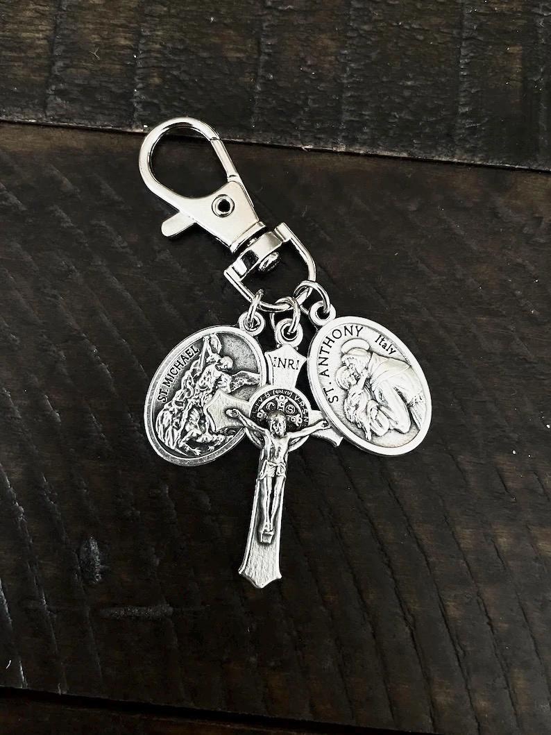 K&ouml;nnte beinhalten: Silberfarbener religi&ouml;ser Schl&uuml;sselanh&auml;nger mit einem Kruzifix und zwei Medaillons. Eines zeigt St. Michael, das andere St. Antonius. Der Schl&uuml;sselanh&auml;nger hat einen Karabinerverschluss. Das Kruzifix tr&auml;gt die Buchstaben INRI.