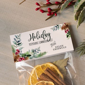 May include: A clear plastic bag filled with a holiday potpourri simmering kit. The kit includes dried orange slices, cinnamon sticks, bay leaves, and star anise. The bag has a white label with the text "Holiday Potpourri Simmering Kit" and "From Helen Griswold".