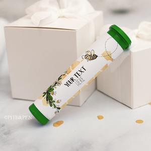 Könnte beinhalten: Eine grüne und weiße Tube mit einem Bienen- und Wabenmuster. Die Tube trägt den Text "YOUR TEXT HERE".