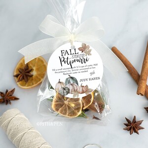 May include: A white circle label with the text "FALL STOVETOP POTPOURRI" and instructions for use. The label is attached to a clear plastic bag filled with dried fruit, cinnamon sticks, and star anise. The bag is tied with a white ribbon.
