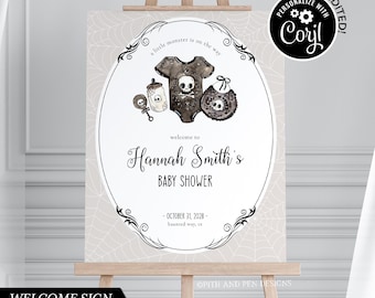 May include: A white welcome sign with a black border and a spiderweb pattern. The sign says "a little monster is on the way" and "welcome to Hannah Smith's Baby Shower". The date is October 31, 2028. There is a black and white illustration of a baby onesie, a bottle, a rattle, and a bib.