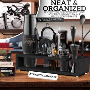 May include: Black bar tool organizer with a variety of tools, including a shaker, jigger, muddler, strainer, and stirrers. The organizer has a black wooden base and a black metal frame. The text "Prodigy Mix" is printed on the shaker.