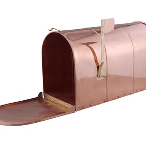 May include: A copper mailbox with an open door, revealing the interior. The mailbox has a curved top and a flag on the side. The door is oval-shaped and has a small hook. The mailbox is made of shiny copper.