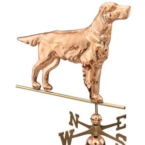 May include: Copper weather vane featuring a standing dog with a compass rose and directional arrows. The dog is facing right and has a long tail. The compass rose is in the center of the vane and has the letters N, S, E, and W.