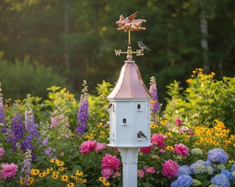 May include: A white birdhouse with a copper roof and a flying pig weathervane. The birdhouse is surrounded by colorful flowers, including pink peonies, purple delphiniums, and yellow wildflowers. A bluebird perches on the weathervane.