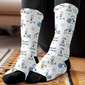 May include: White crew socks featuring a repeating pattern of stick figures performing physical therapy exercises, including using exercise balls, steps, and resistance bands, with the text Physical Therapy and Difference Makers printed in blue.