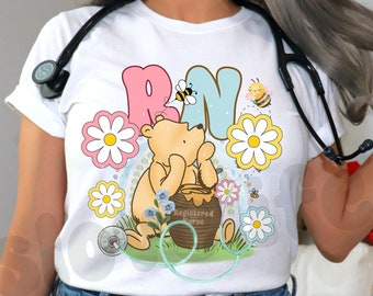 May include: A white, light blue, and pink t-shirt with a cartoon Winnie the Pooh character holding a jar of honey. The shirt has the letters "RN" in a stylized font and features a stethoscope and flowers. The text "Registered Nurse" is on the honey jar. The t-shirt is available in three colors: white, light blue, and pink.