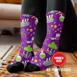 May include: A pair of purple socks with a science-themed pattern. The socks feature illustrations of beakers, test tubes, atoms, and other lab equipment. The socks have the text "UNISEX SIZE" and "#6: FUNNY SCIENCE" on them.