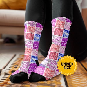 May include: A pair of knee-high socks with a colorful, geometric pattern in shades of pink, purple, red, and blue. The socks have black toes and heels. A yellow sticker with the text "UNISEX SIZE" is visible.