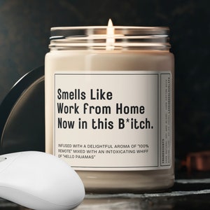 May include: A white candle with a black label that reads "Smells Like Work From Home Now in this B*tch." The label also includes the text "Infused with a delightful aroma of "100% Remote" mixed with an intoxicating whiff of "Hello Pajamas."