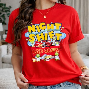 May include: A red t-shirt with the words "NIGHT SHIFT LAB CREW" in a yellow and blue design. The graphic includes cartoon lab creatures and lab equipment. The shirt is short-sleeved.