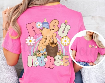May include: Pink t-shirt with a Winnie the Pooh design and the text "MCU Nurse" in a retro font. The design features Winnie the Pooh holding a jar of honey and a baby bottle. There are daisies and a rainbow in the background.