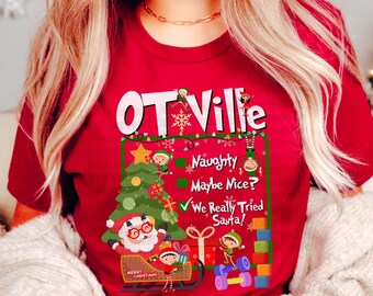 May include: A red t-shirt with a Christmas-themed graphic. The graphic includes the text "OT Ville", a Christmas tree, Santa Claus in a sleigh, and the phrases "Naughty", "Maybe Mice?", and "We Really Tried Santa!"