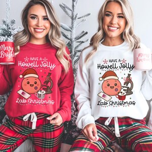 May include: Red and white Christmas sweatshirts with the text "Have a Howell Jolly Lab Christmas" and a cartoon cell wearing a Santa hat. The models are wearing red and green plaid pajama pants and holding mugs that say "Merry Bright".