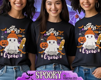 May include: Three women wearing black t-shirts with a Halloween-themed graphic. The design features a ghost wearing a hat, holding a pencil, and a pumpkin. The text on the shirt reads "The Spooky Para Crew". Below the women is a banner that reads "Spooky Personalized Paraprofessional".