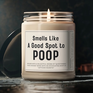 May include: A white candle with a black label that reads "Smells Like A Good Spot to POOP". The label also includes the text "Infused with a delightful aroma of "questionable food choices" mixed with an intoxicating whiff of "leftover regrets!"