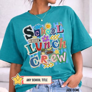 May include: Teal t-shirt with the words "School Lunch Crew" in colorful, playful lettering. The design includes a sun, flowers, and a lunch tray graphic. The bottom of the shirt has a banner that says "ANY SCHOOL TITLE".
