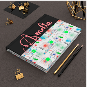 May include: A black and white notebook with a colorful science pattern on the cover. The notebook has a black spine and the name "Amelia" is written in pink on the front cover.