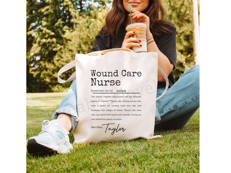 May include: White tote bag with black text that reads "Wound Care Nurse (wund-ker-no-rs) noun The master comfort connoisseur and the ultimate healer of 'ouches'. They're the unsung heroes who have a knack for turning ouch into ah, and bandages into badges of honor. They're the ones who can mend both hearts and wounds, leaving no scar behind but plenty of smiles. See Also: Taylor"