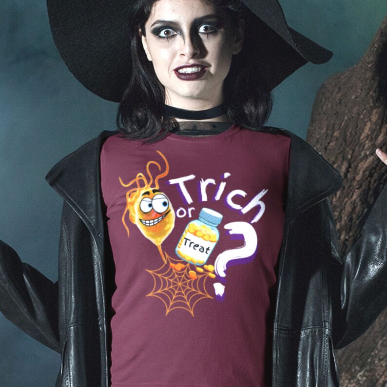 以下が含まれることがあります： ハロウィーンをテーマにしたバーガンディ色のTシャツ。デザインは、笑顔の漫画の細菌、"Treat"と書かれた薬瓶、クモの巣、"Trick or ?"の文字が特徴です。黒い服を着た人が着用しています。