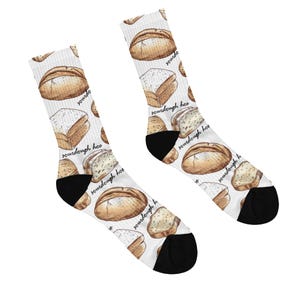 May include: A pair of white socks with a repeating pattern of watercolor-style sourdough bread loaves and slices. The socks have black heels and toes, and the words "sourdough hoe" are printed on the socks.