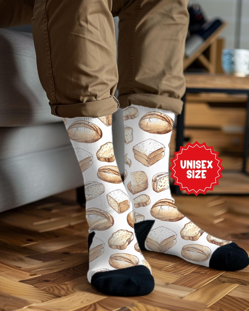 May include: White socks with a repeating pattern of various bread loaves and slices in shades of brown. The socks have black heels and toes, and a red "UNISEX SIZE" sticker is visible.