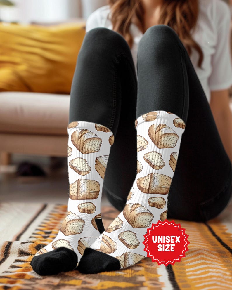 May include: White socks with a repeating pattern of illustrated bread loaves and slices. The socks have black toes and heels. A red sticker with the words "UNISEX SIZE" is visible.