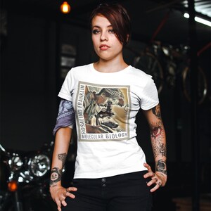 May include: White t-shirt with a vintage-style illustration of Rosalind Franklin, a scientist, looking through a microscope. The text "Rosalind Franklin" and "Molecular Biology" is printed on the shirt.