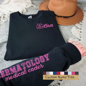 May include: Black sweatshirt with pink text that reads "DERMATOLOGY medical coder" on the sleeve and "Lisa" with a pink skin and hair icon on the front.